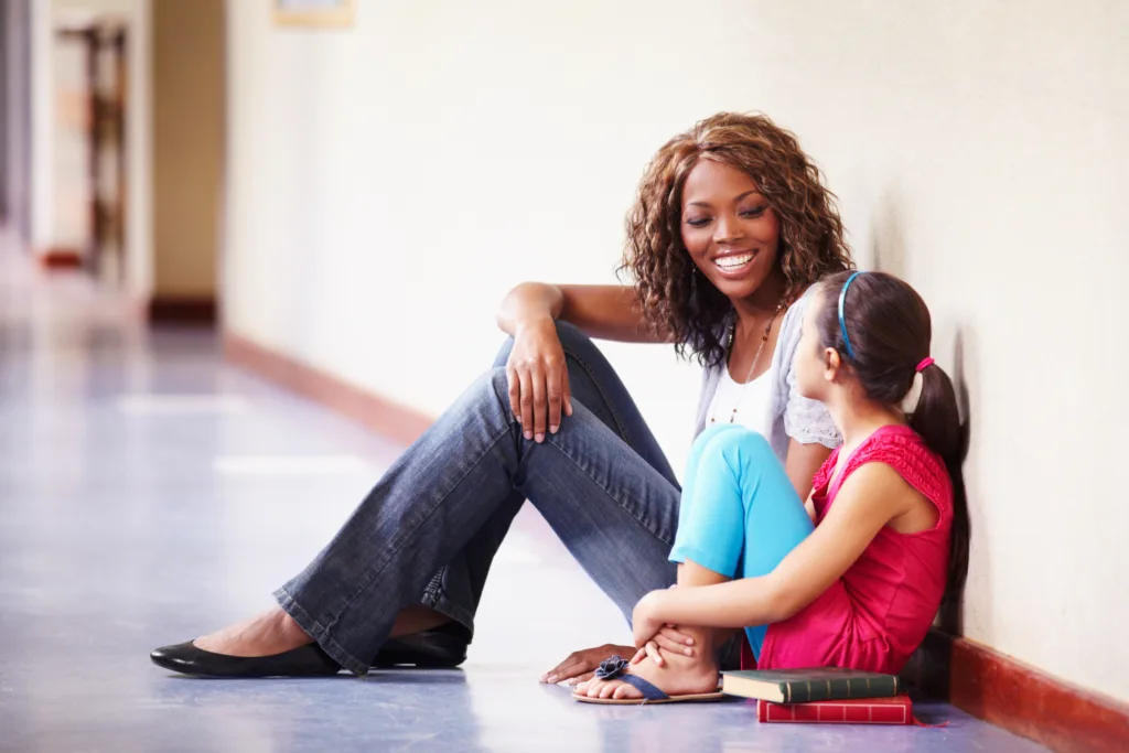 Teacher and young student sitting in hallway talking