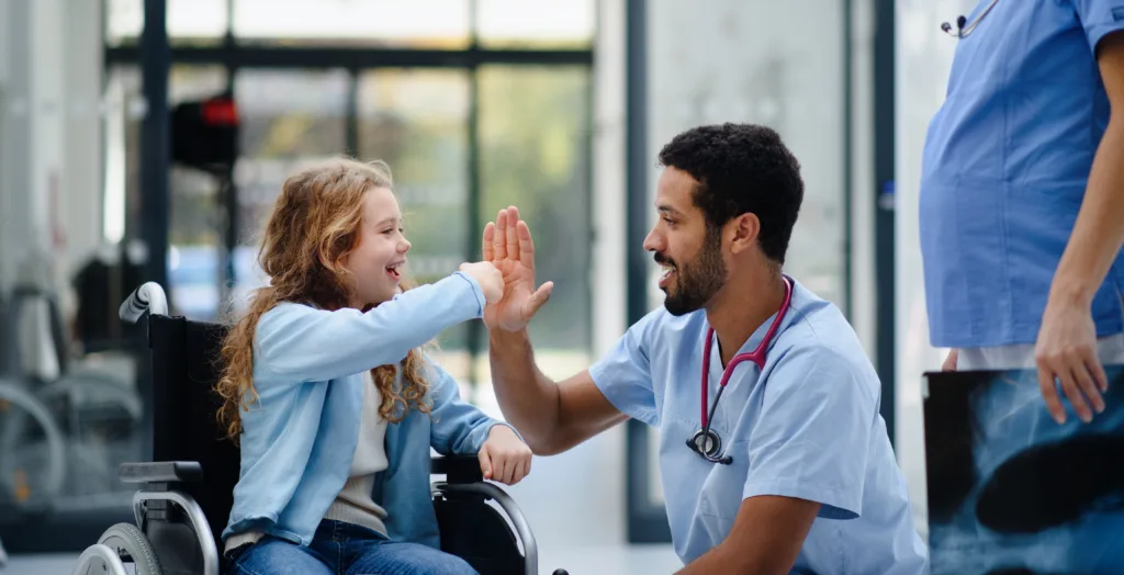 Male doctor giving high five to girl in wheel chair