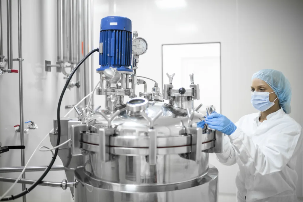  young female skilled worker in protective gear operates a high-tech equipment in a pharmaceutical production facility, ensuring the precise mixing of substances to 