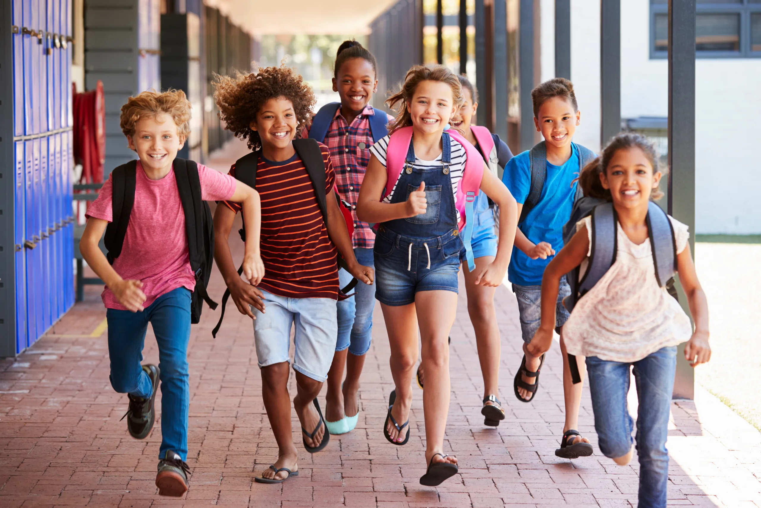 Young child students running down school hallway smiling with backpacks on