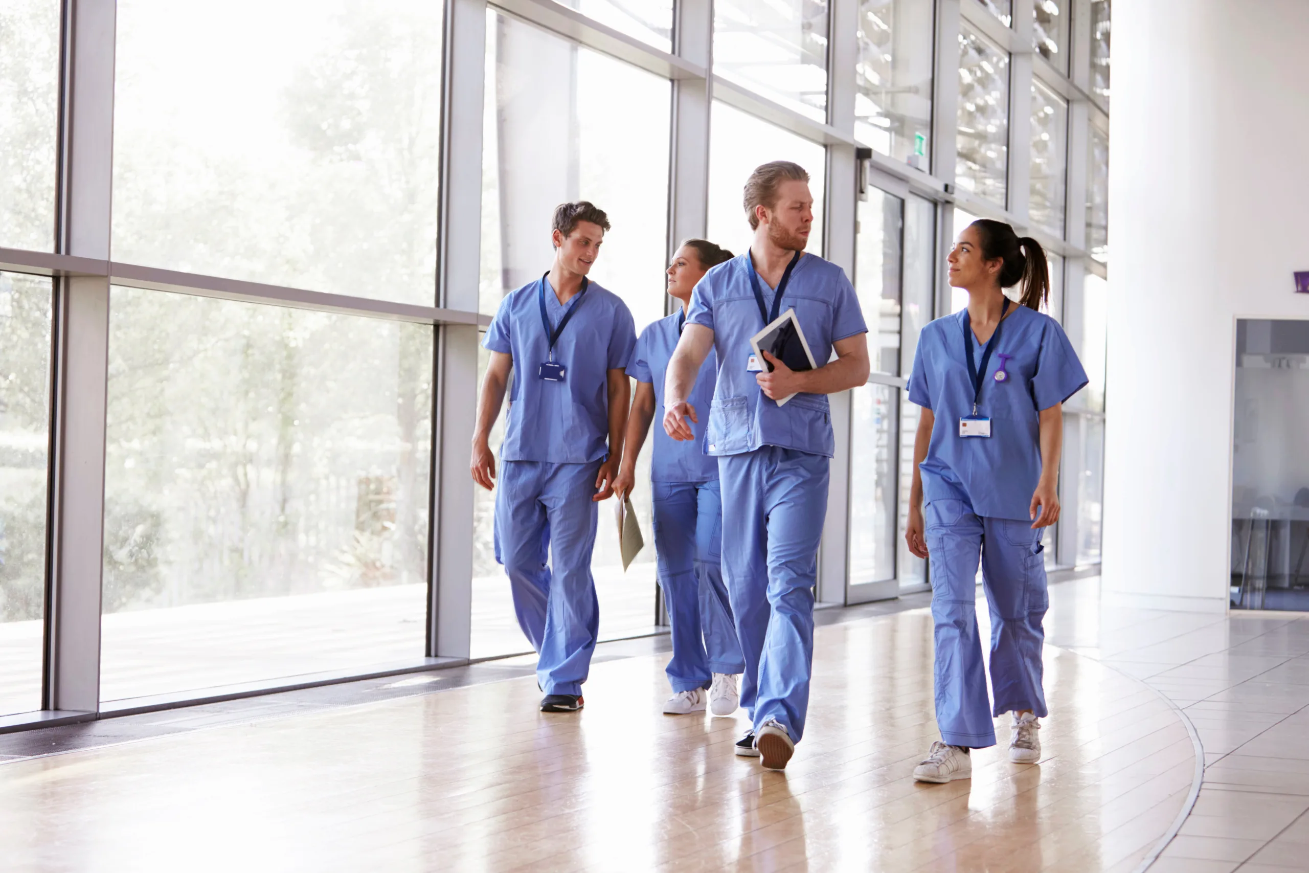 Four healthcare workers in scrubs walking in corridor