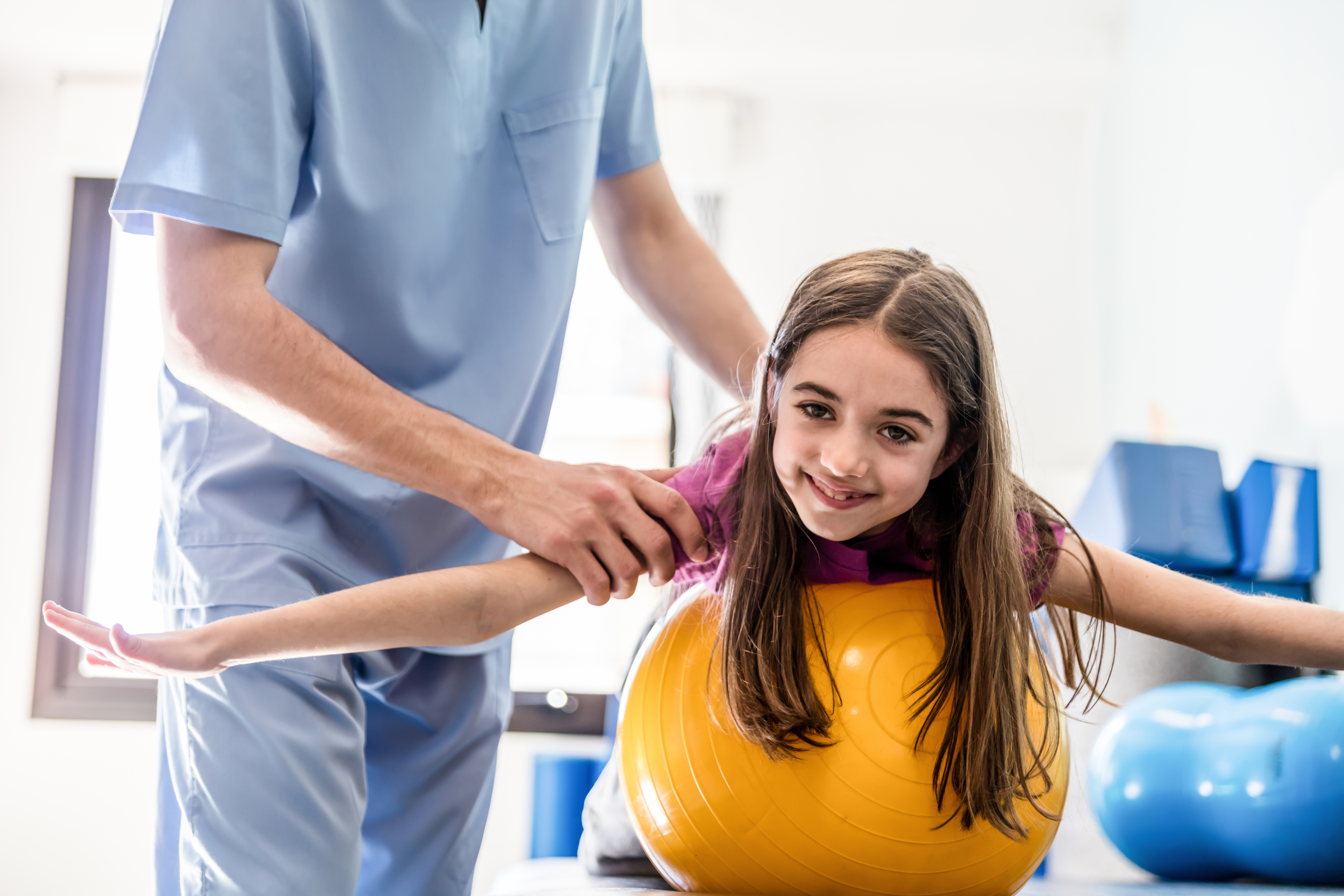 Young girl at occupational therapy leaning on a ball on tummy smiling very happy