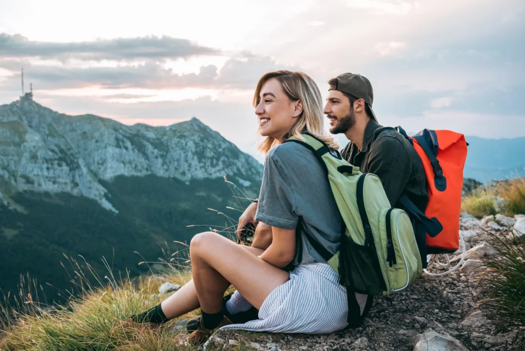 Male and female sit on a cliff enjoying the views of the mountains on their travels