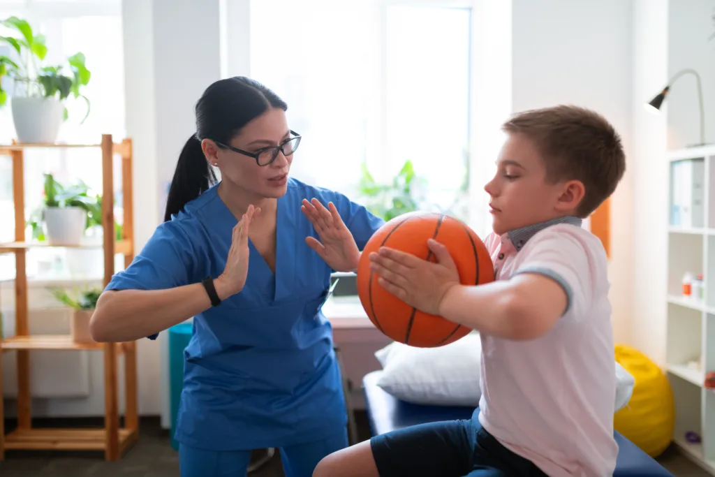 Nurse in blue uniform showing example of exercise with ball to young boy