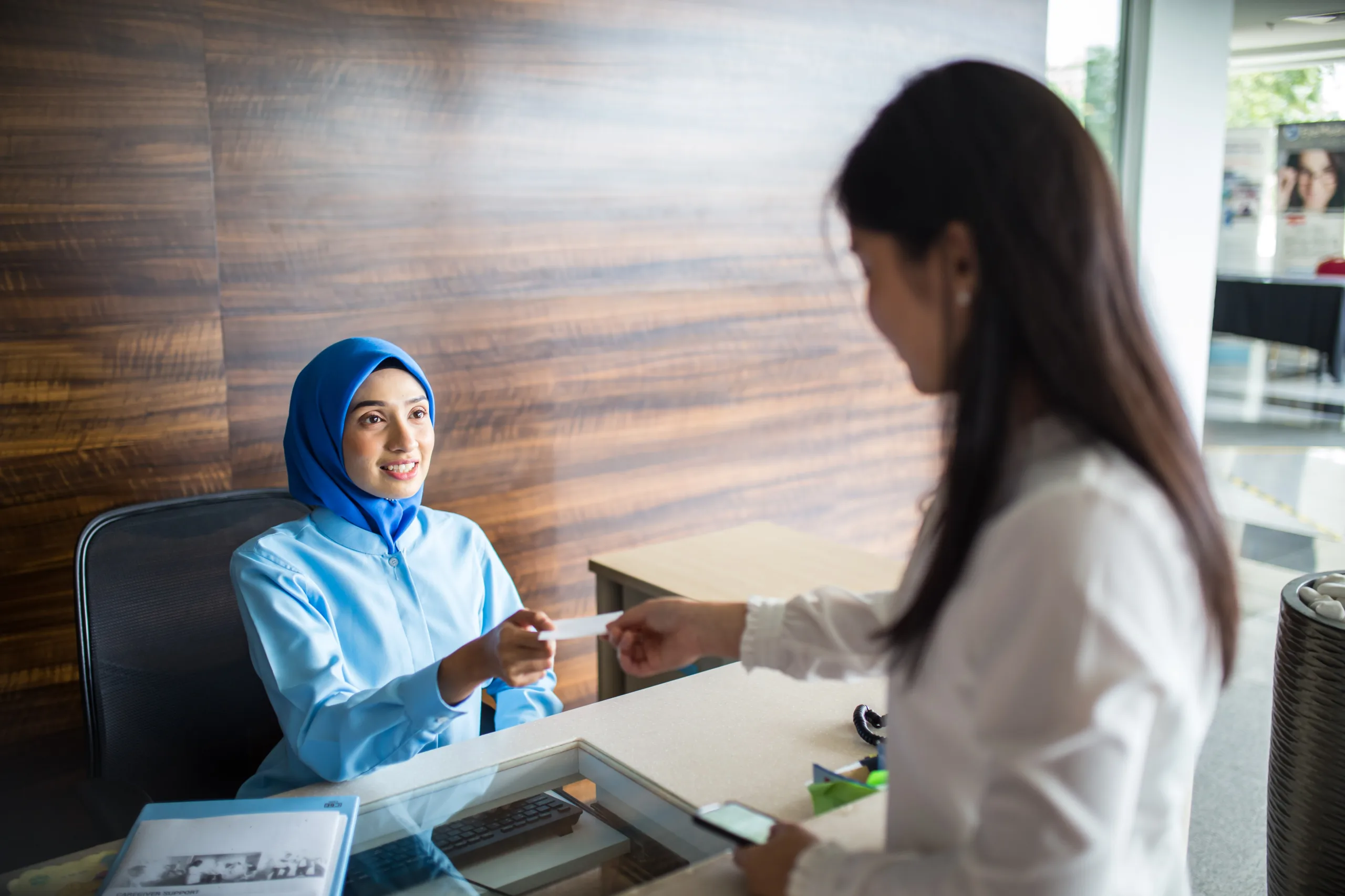 Medical staff assisting female patient at hospital reception desk,