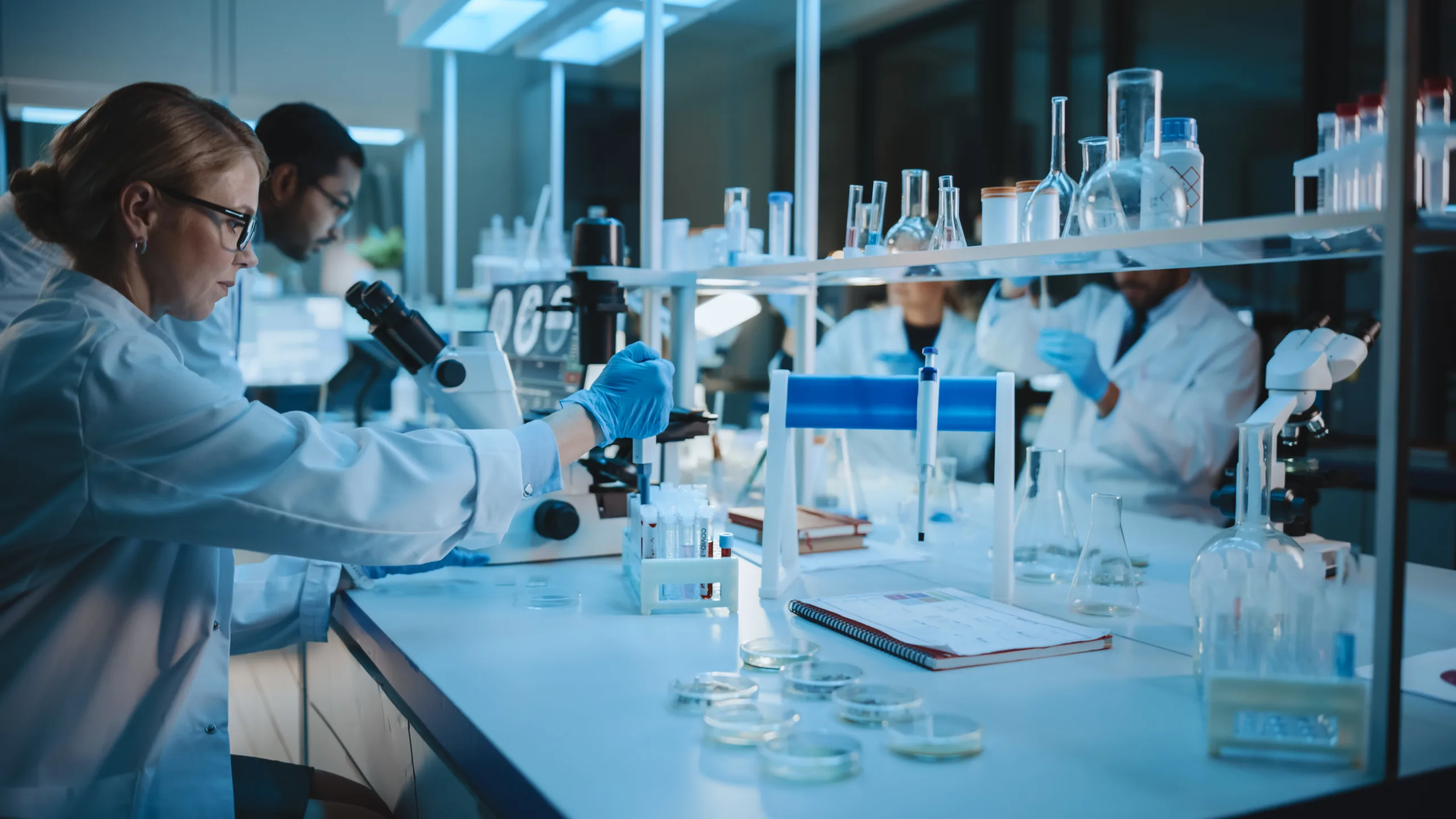 Team of Medical Research Scientists Work using Microscope, Test Tubes, Micropipette and Writing Down Analysis Results. Laboratory Looks Busy, Bright and Modern.