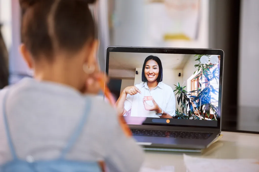 Young student on a video call with her teacher doing a virtual lesson on speech therapy