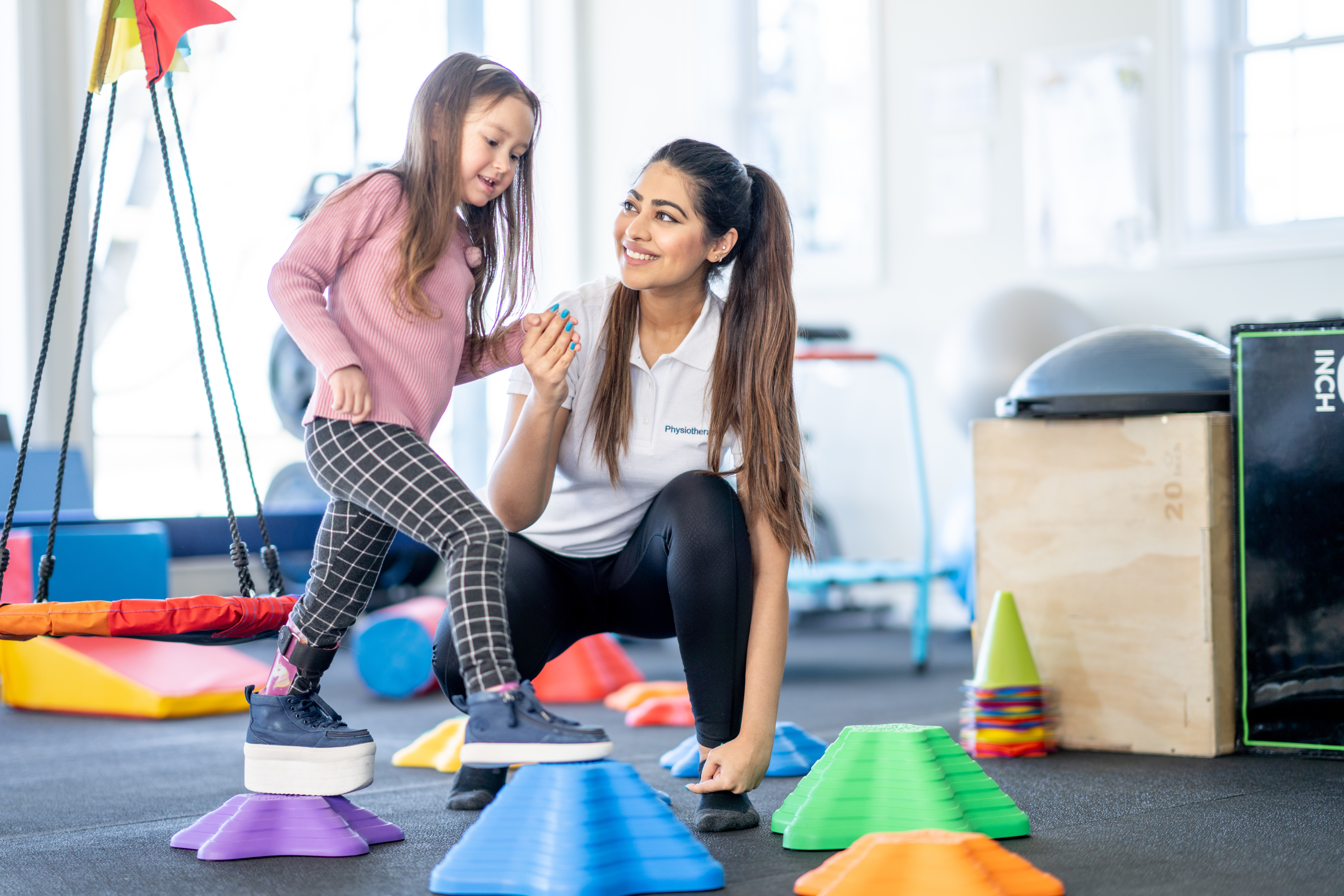 Young girl holding physical therapists hand as she works on her balance with her brace on