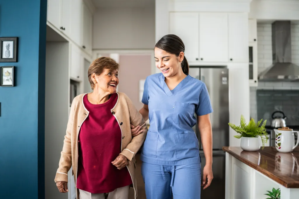 Home caregiver helping senior woman to walk at house