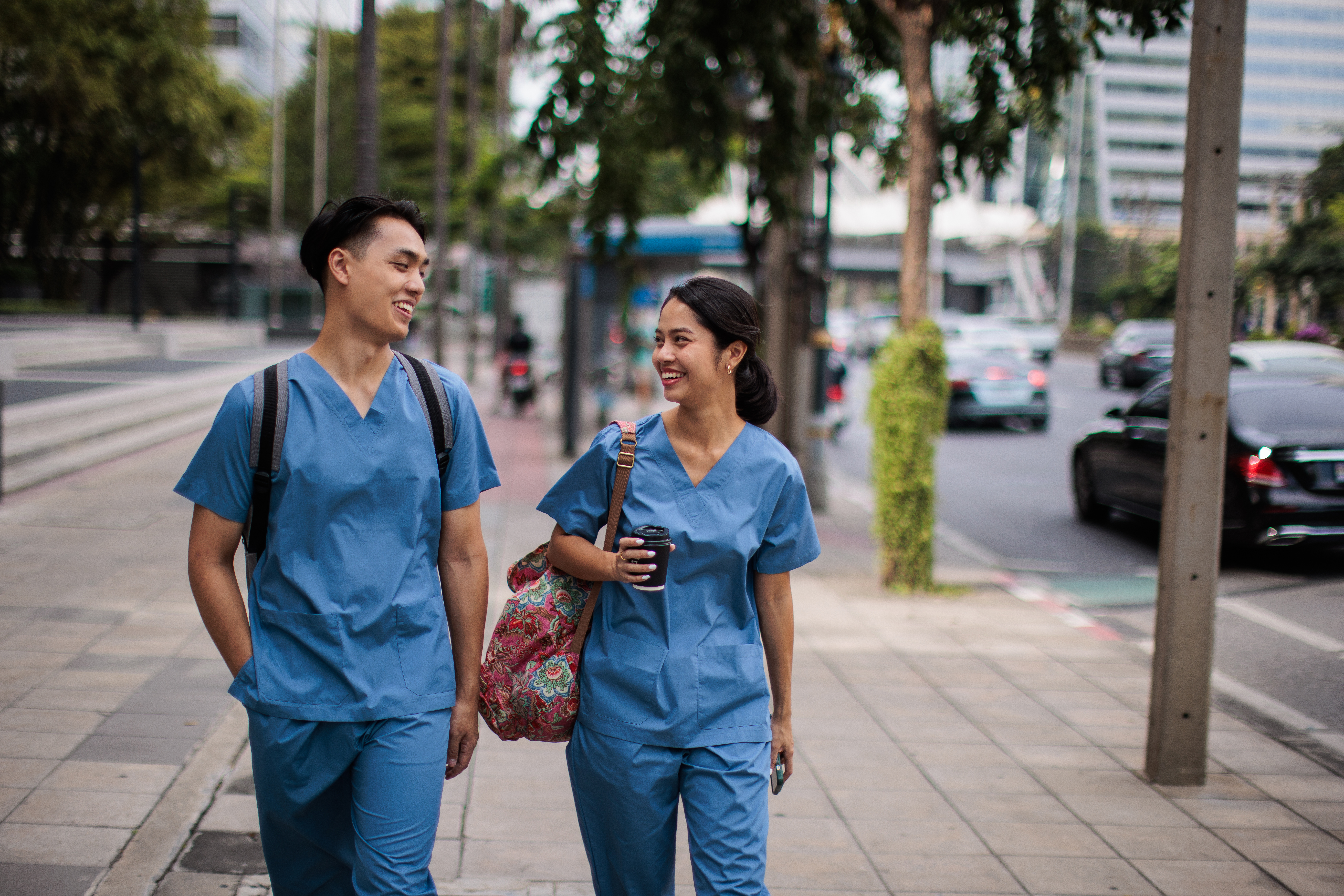 Man and woman healthcare workers in medical scrubs walking to work on the street together.