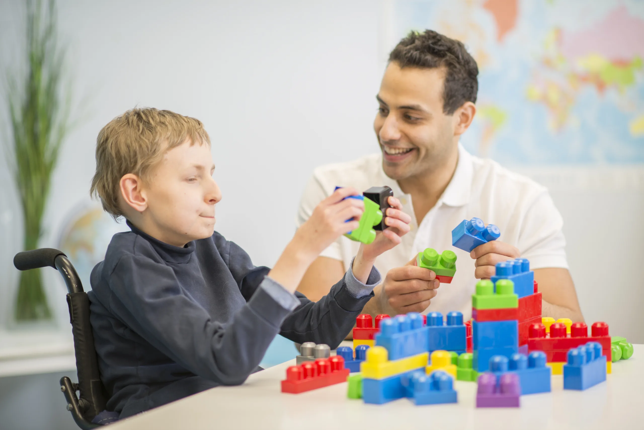 A caregiver is helping a boy with cerebral palsy work on building a block tower for hand eye coordination.