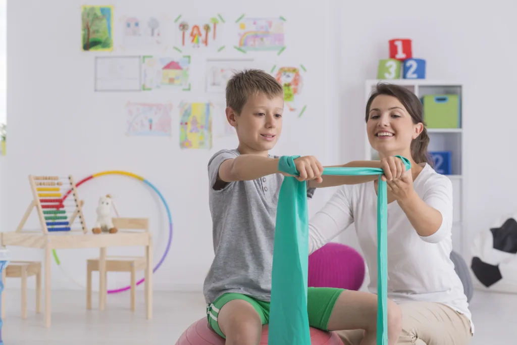 Physiotherapist and young boy sitting on a gym ball
