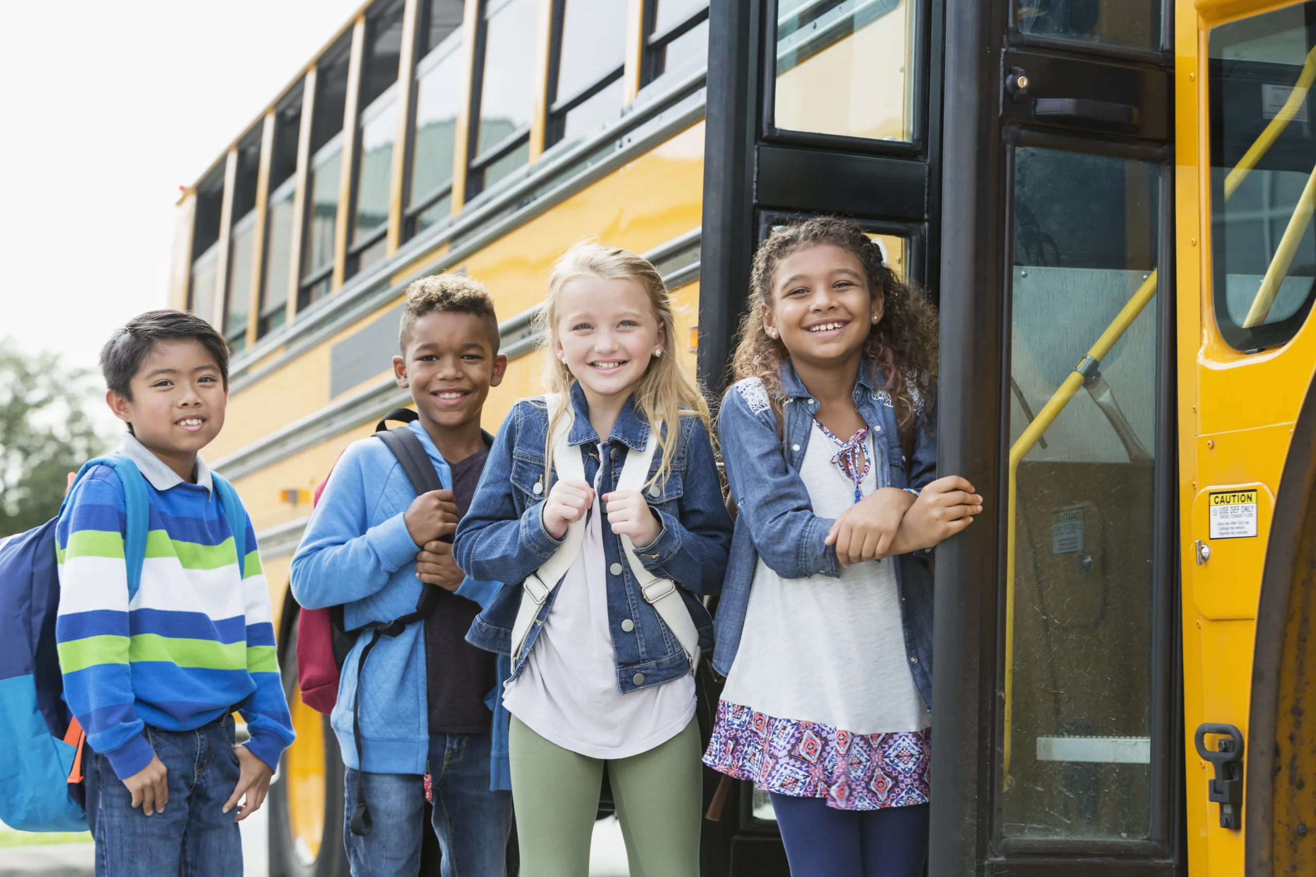 Young students with backpacks smiling about to board the yellow school bus
