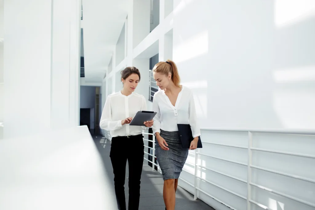 Two female professionals walking down hallway looking at data