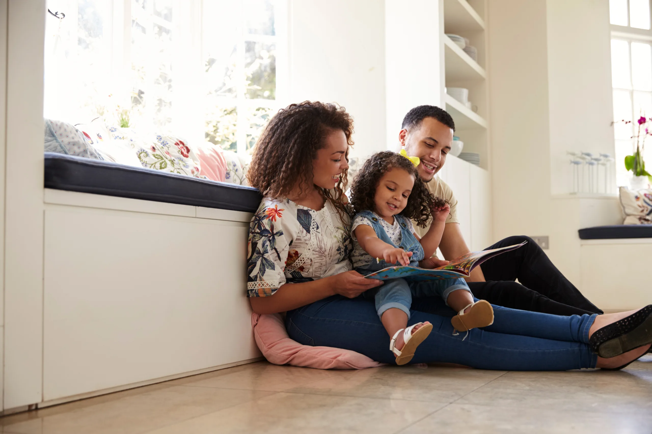 Parents and their daughter sitting on the floor reading book
