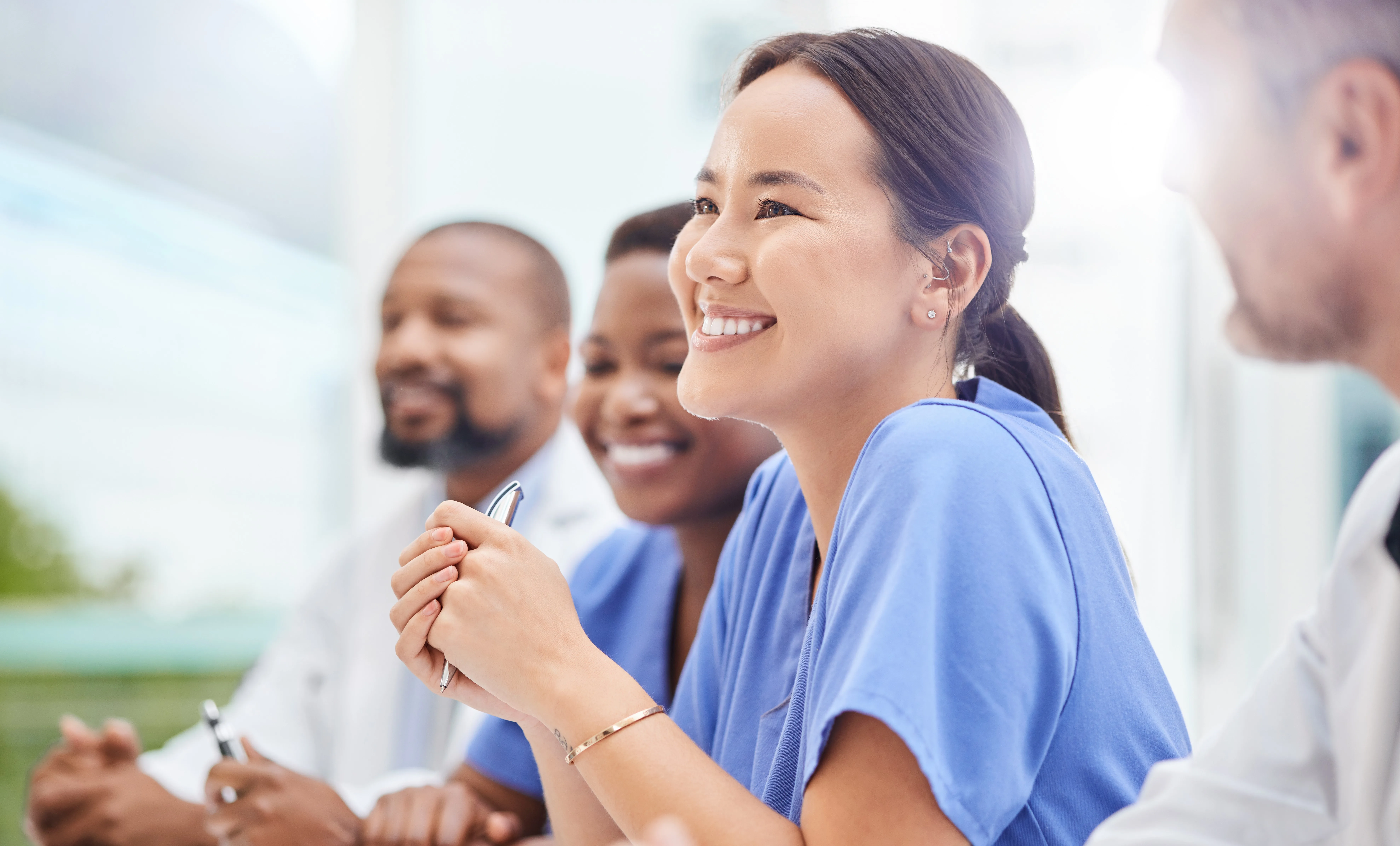 A group of diverse healthcare professionals in scrubs and white coats smiling during a wellness-focused team meeting—highlighting collaboration, positivity, and support in the medical field.